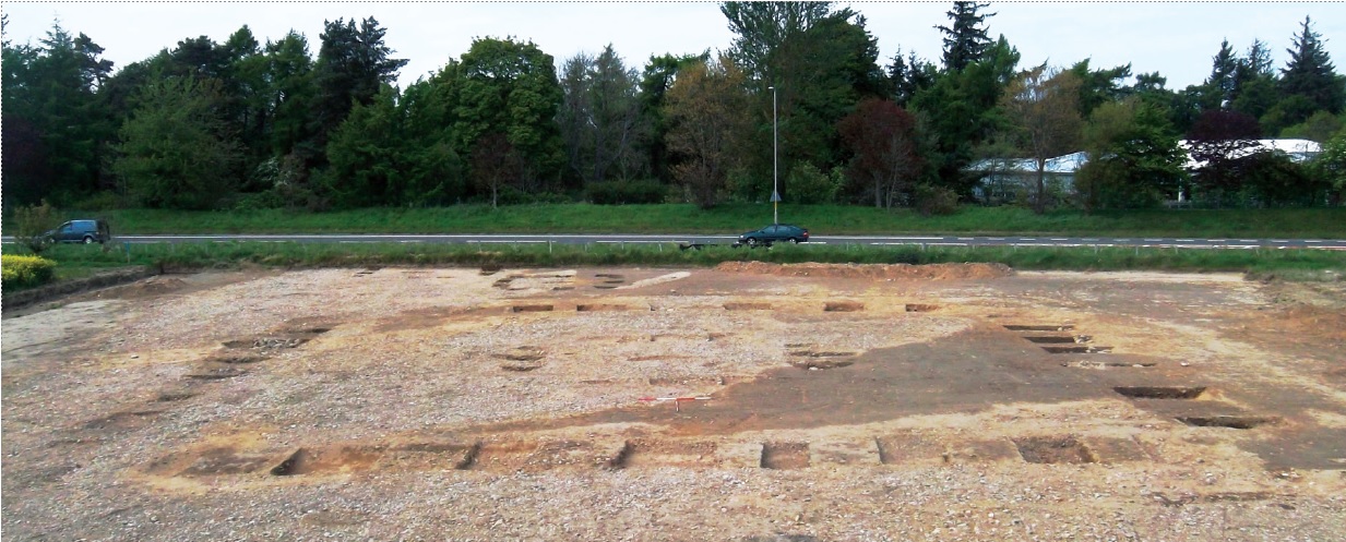 Photo showing the archaeological excavation of the large Pictish square barrow at Greshop, near Forres. The early medieval route likely passed by here, just as the A96 in the background does today 