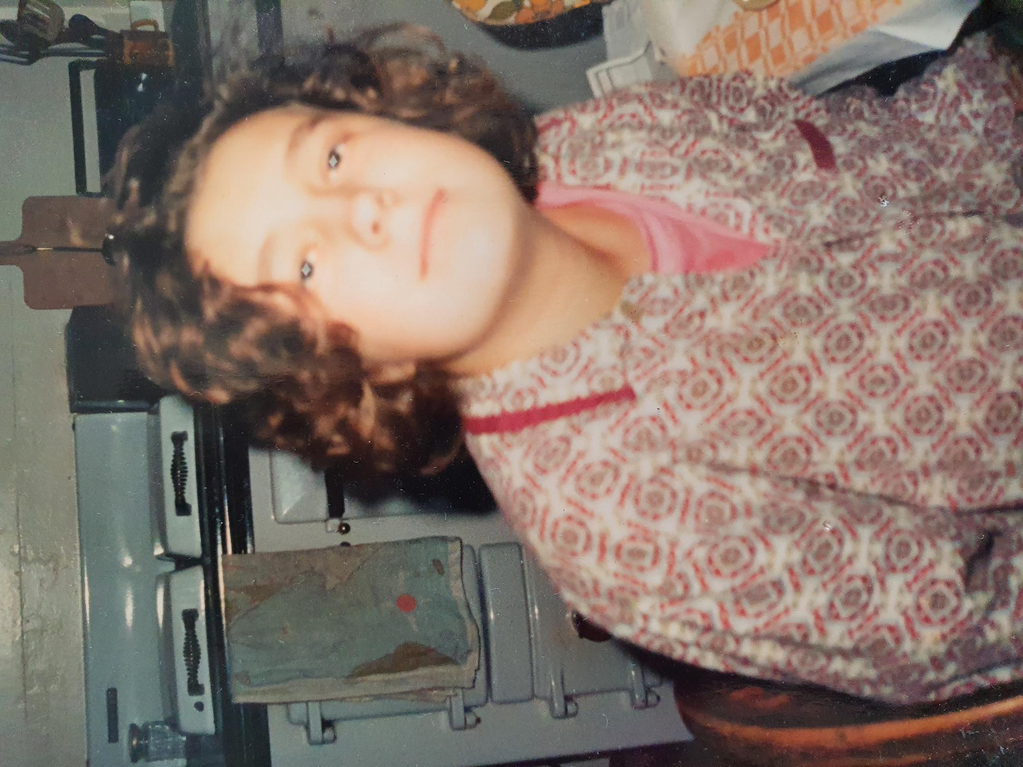 Photo of me aged 17, at the breakast table, wearing a pink t-shirt and a pair of my dad's pyjamas. I am staring into the camera with a vaguely faraway look.