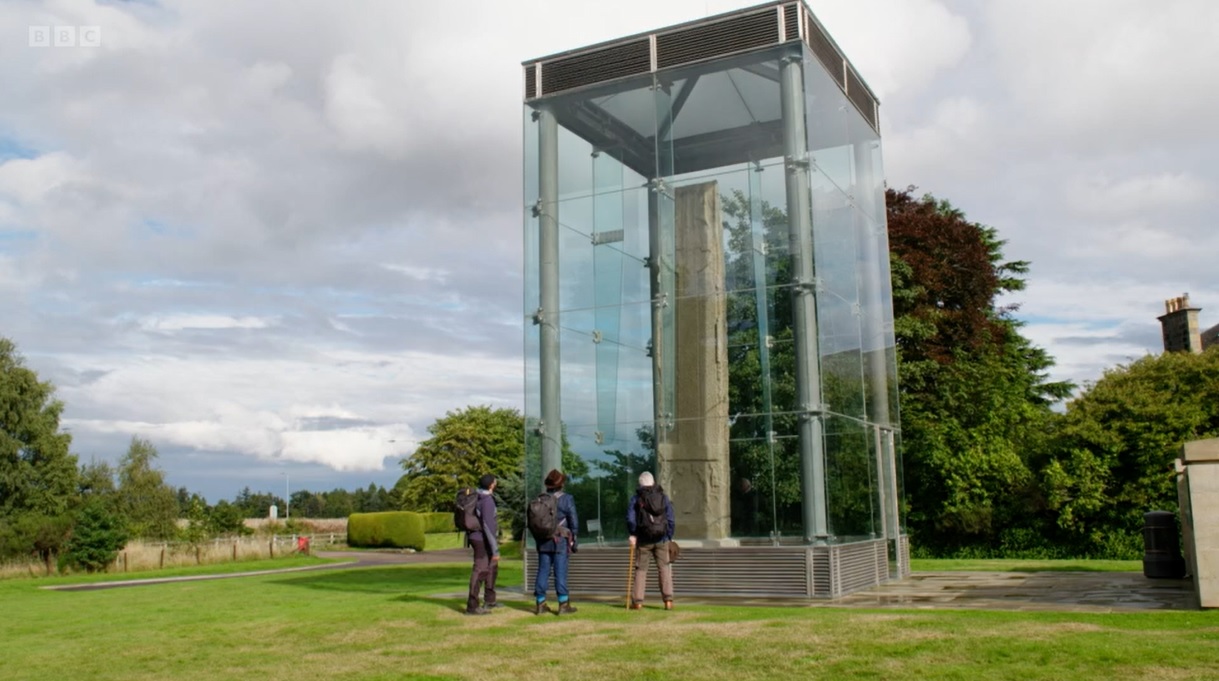 Still image from episode 3 of the BBC programme Pilgrimage: The Road to the Scottish Isles. Monty Panesar, Laurence Llewelyn Bowen, and Nick Hewer look up at the cross face of Sueno's Stone.